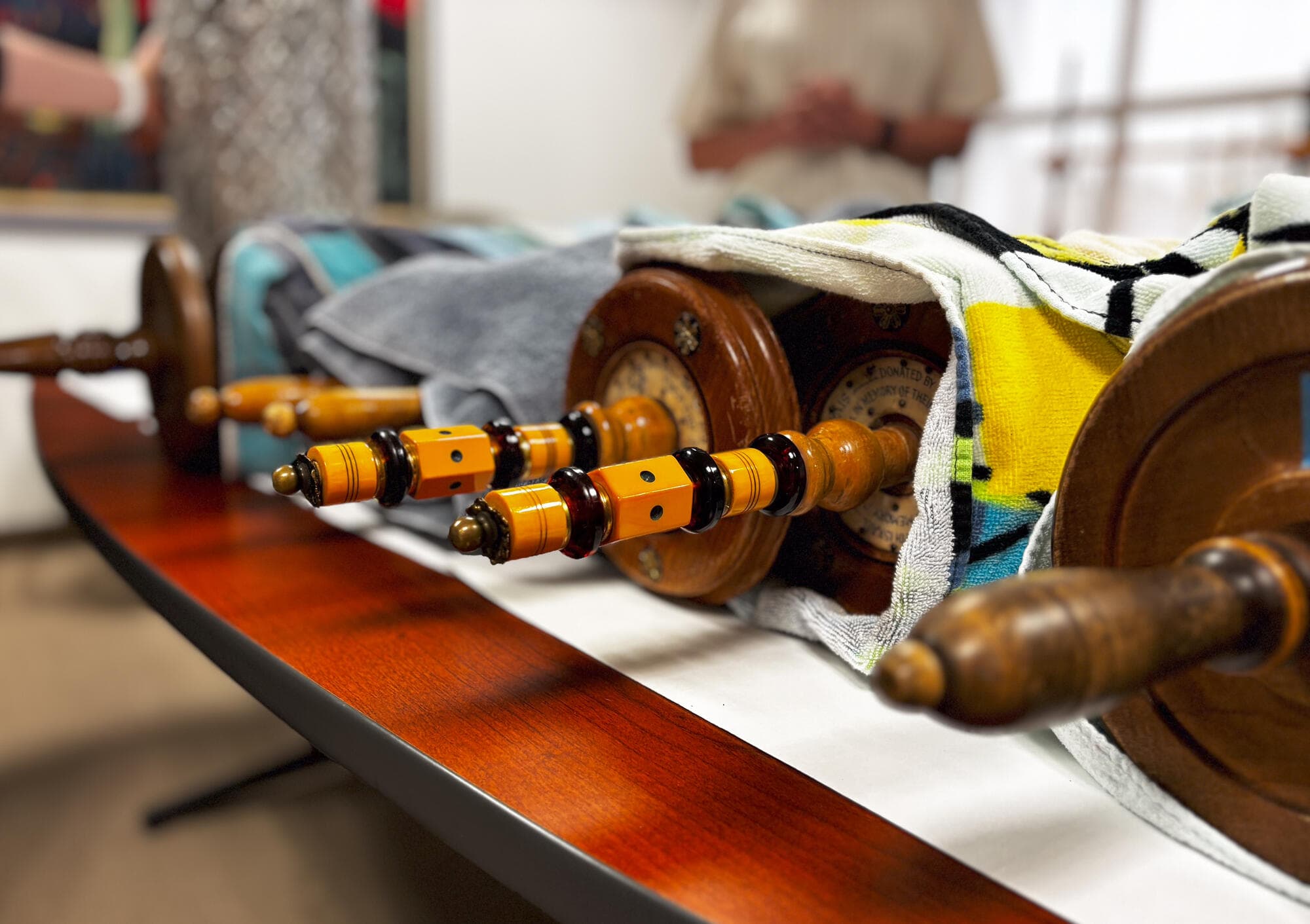 Decorated handles jut out from torah scrolls wrapped in towels sitting on a table.