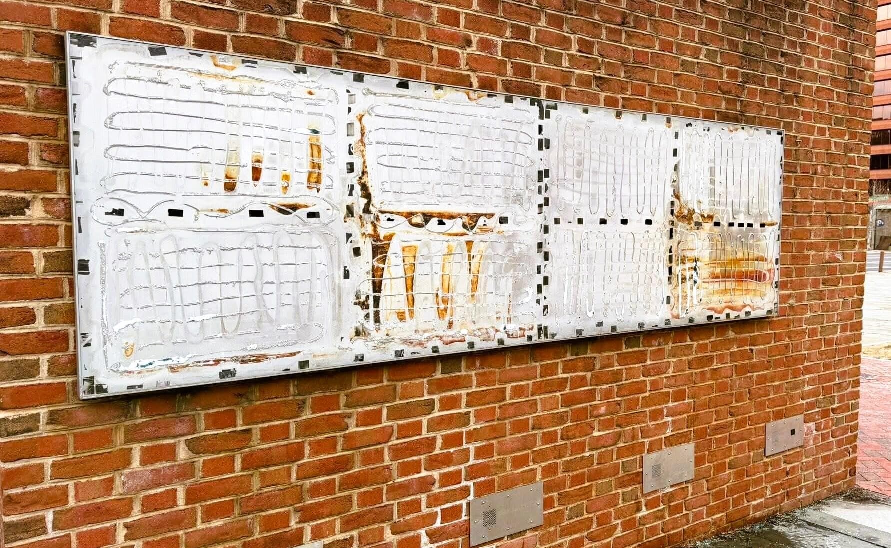 Image of a brick wall with a bare mounting foundation showing lines of adhesive that once held museum signs in place.