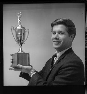 Two men in an office - one with a trophy
