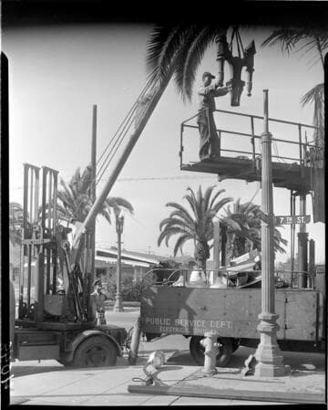 Man on scaffold mounting top of double streetlight to standard