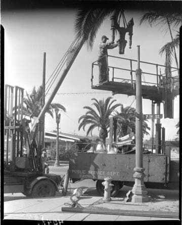 Man on scaffold mounting top of double streetlight to standard