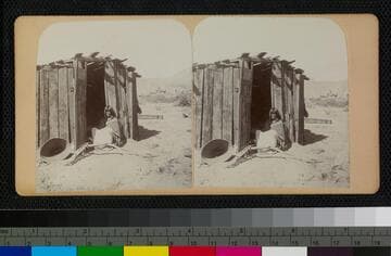 Hualapai Indian woman in doorway of house.  A large basket is at the left
