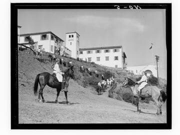 Boys riding horses toward campus buildings, Urban Military Academy, Brentwood, Los Angeles