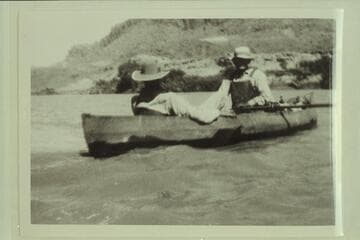 George C. Fraser sitting in the stern of one of Dave Rust's folding canvas boats.  Glen Canyon.  Bert Loper is at the oars as boatman for Rust