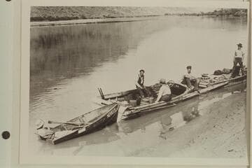 Nevills sitting in a fold-flat boat trailing two makeshift motorboats on the Colorado River at Moab