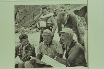Briefing at Diamond Creek. Hugh Cutler sits lower left. Rod Sanderson and Marston work on the details from the charts. Buzzy Belknap indicates that all the talky-talk gives him a pain. Masland appears to find it interesting