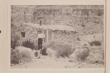 E. E. Spencer standing in front of Mendenhall cabin on the San Juan River. E. E. Spencer had come down from Salt Lake to visit Arthur Spencer at his trading post at Mexican Hat