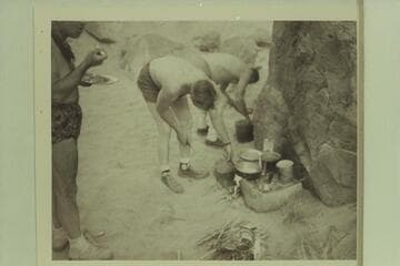 Breakfast at camp at Mile 19, right bank.  Marston stands at left.  Edward Hudson and Willie Taylor dish up the mix