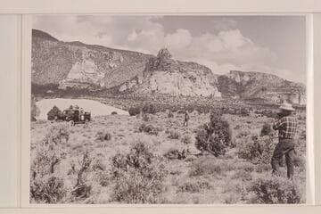 The sandstone butte near the foot of Navajo Mountain.  Jorgen Visbak and Frank Masland sit in the Power Wagon.  Bahe stands center and Bill Belknap tries for a pictures.  War God Spring would be about at upper left of picture