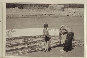 Norm Nevills repairing boat (?) after hitting rock, probably Nokai (?) Rapids. Jackie Frost watches