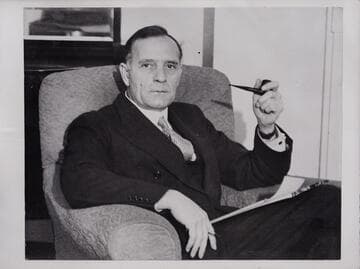 Portrait of Edwin Powell Hubble, seated in a chair, holding a pipe