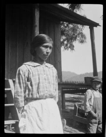 Native American woman and young boy next to house