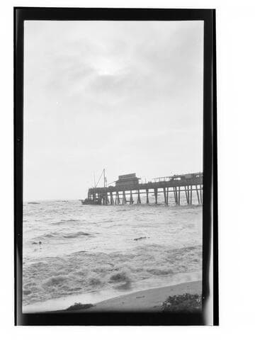 Short pier seen from shore with boat and people at end