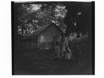 A group of five children standing in front of wooden house