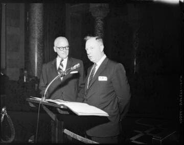 Two men at podium, one is speaking