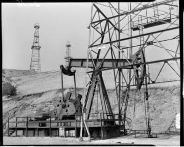 Oil well pumping in foreground with derricks in the back
