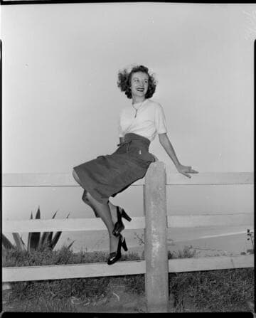 Young lady in a skirt sitting on a fence rail overlooking the beach
