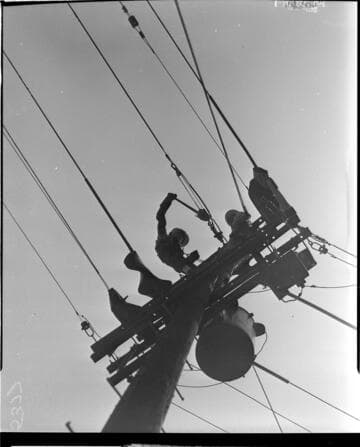 Looking up at lineman tensioning conductor at top of pole