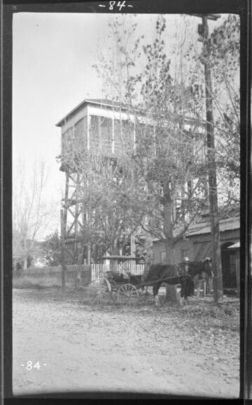 Side view of the Tulare substation and waterworks with a horse buggy and two people standing in the foreground