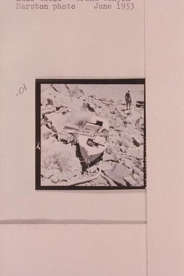 The Russell-Tadje boat "Ross Wheeler" on left bank above Bass Cable, Grand Canyon. Mile 108. Note the patches on the bow repairing the hole punched by a falling rock below Pipe Creek. Claude Nichols is in background