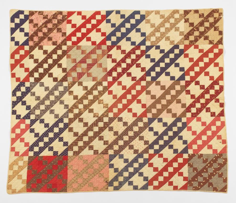 Quilt with Jacob’s Ladder pattern in red, pink, cream, tan, and brown.