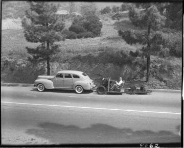 Man parking the 3 wheel vehicle without a body behind another car. The single rear wheel is the one that turns