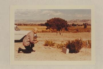 Dock Marston at the grave of Frank V. Goodman. The wooden markers in the background are the graves of Nat Galloway and his wife. Vernal Cemetery