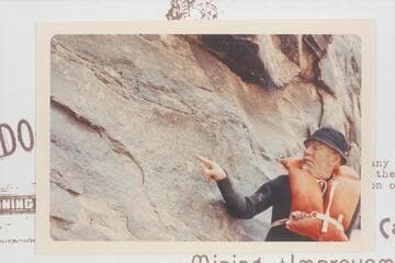 Dock Marston posed at the D. Julien inscription at Mile 185.75, Cataract Canyon. A later Visiting group pictured an 1891 inscription to the right of the D. Julien and a part would be aboVe the pointing arm