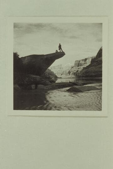 Preston Mercer standing on rock on river side of the mouth of the Escalante River. Sally Van Valkenburg sits on the rock