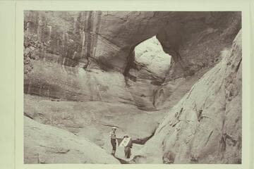 Masland and Marston holding Explorers Club flag at natural bridge in Navajo Canyon. Masland proposes name, "Ba-Sah Bridge," for the seven pot-holes below it
