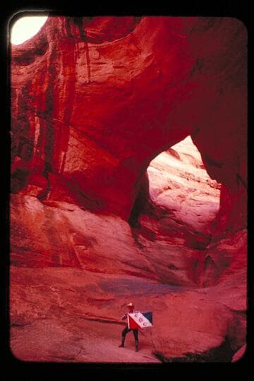 Masland and Marston holding Explorers Club flag at natural bridge in Navajo Canyon. Masland proposes name, "Ba-Sah Bridge," for the seven pot-holes below it