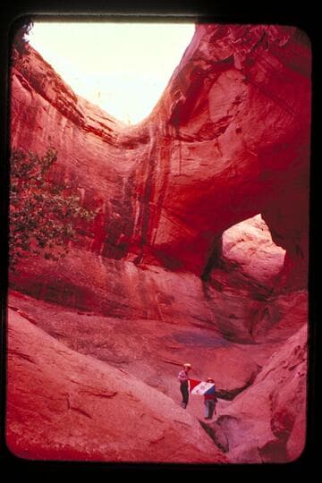 Masland and Marston holding Explorers Club flag at natural bridge in Navajo Canyon. Masland proposes name, "Ba-Sah Bridge," for the seven pot-holes below it