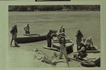 Just before departure from Lees Ferry for Grand Canyon traverse. Masland stands left. Eisaman stands in the "Bootoo." Taylor holds the line of the "Cactus." Visbak stands in the "Cactus." Marston with hands in pockets on beach