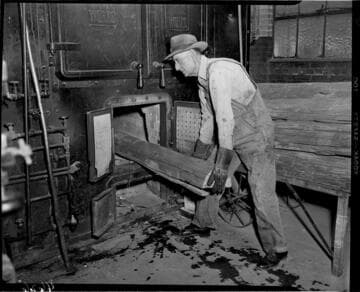 Man is loading split pieces of wood poles into furnace